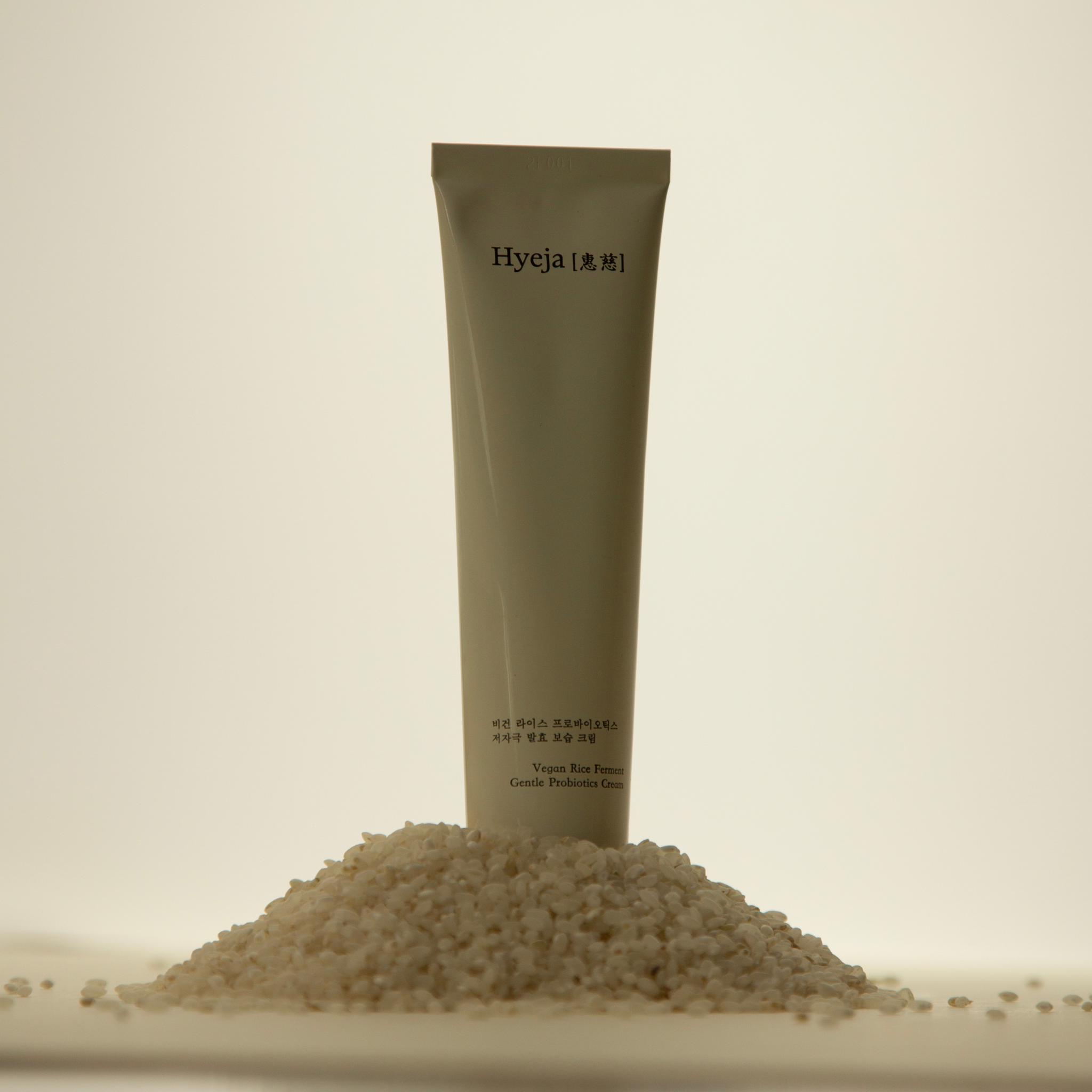 Hyeja Vegan Rice Ferment Gentle Probiotic Cream in minimalist earth-toned tube, artfully positioned with scattered rice grains