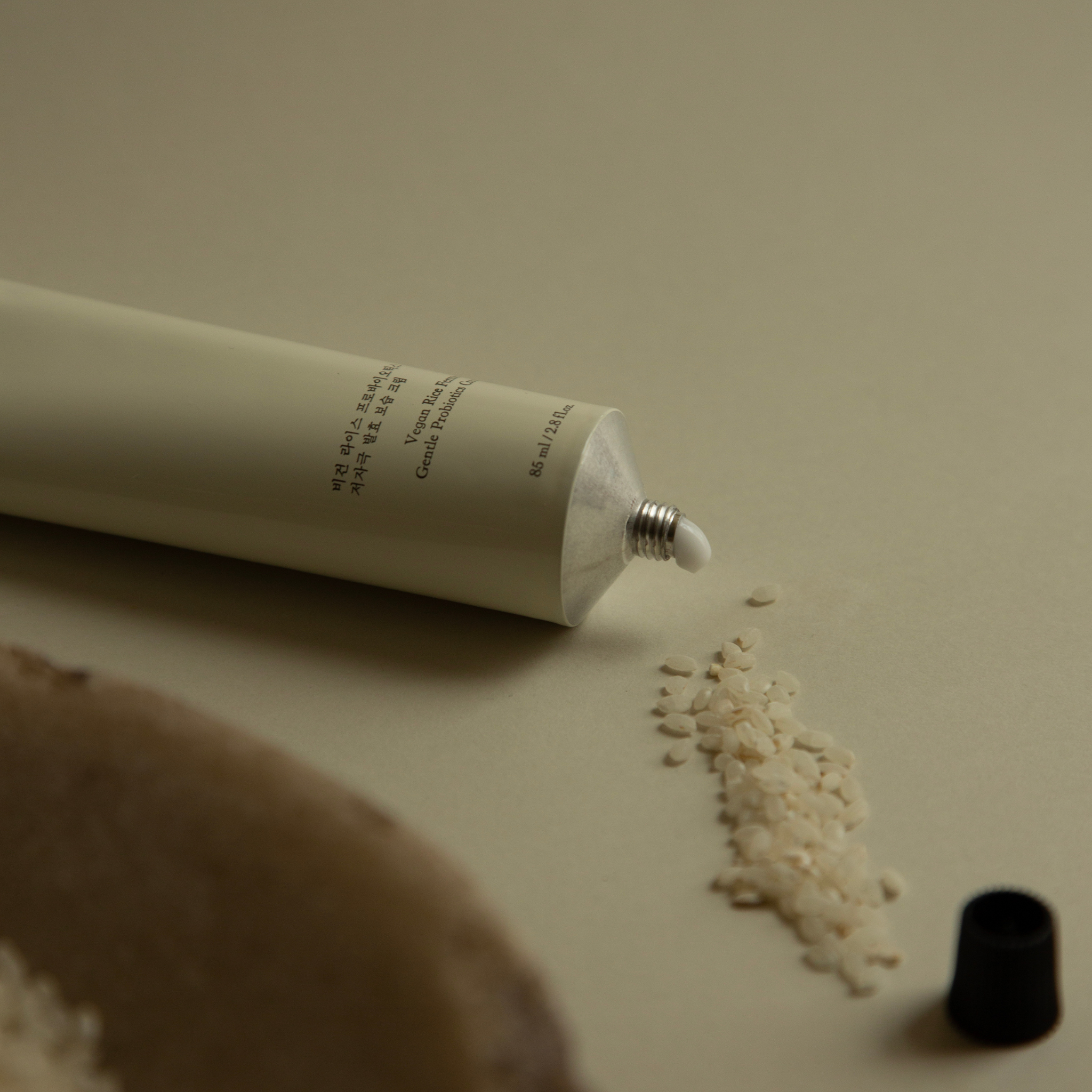Hyeja vegan rice ferment probiotic cream in minimalist white tube, showcasing natural skincare ingredient with scattered rice grains