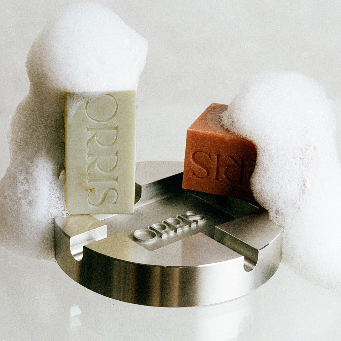 Orris Paris artisanal soap bars with sculptural metal display, surrounded by soft white foam, showcasing minimalist product design and natural texture