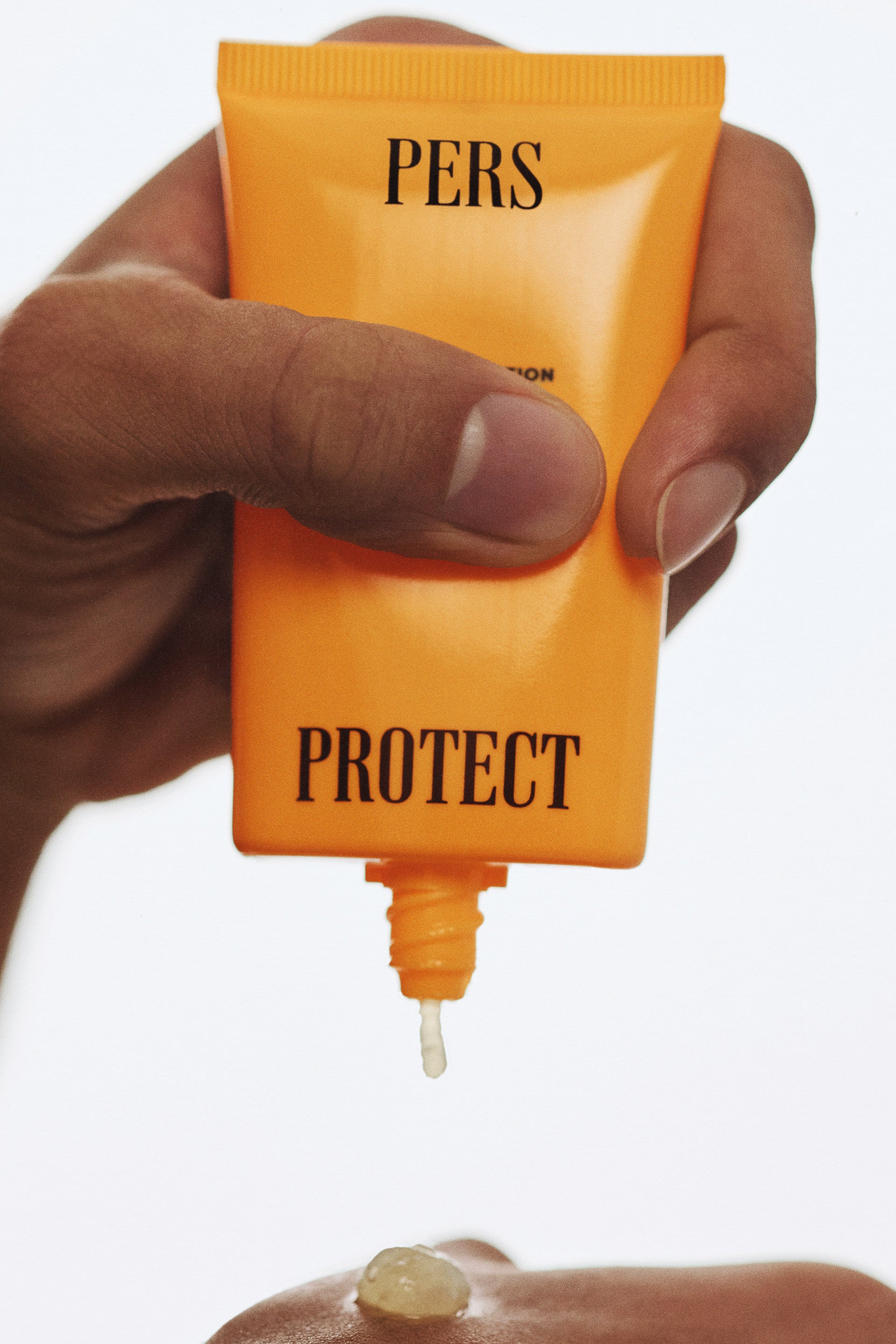 Hand holding PERS SPF 50 sunscreen in a close-up editorial product image