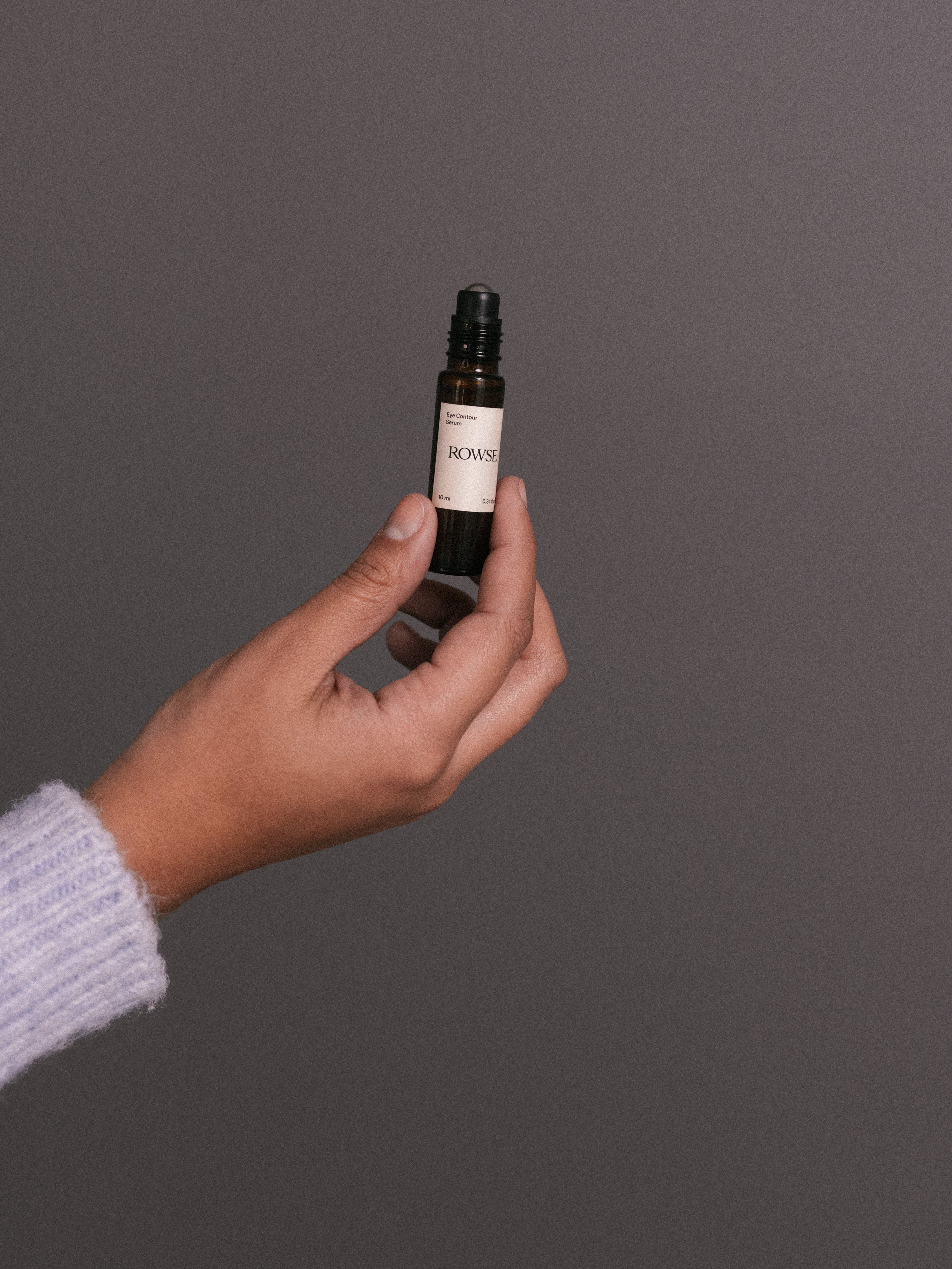 ROWSE Eye Contour Serum roll-on bottle held against neutral background, showcasing minimalist packaging and precise skincare application design