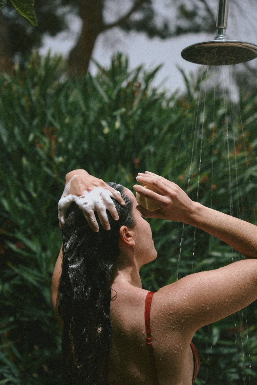 ROWSE hair care product being used in an outdoor shower, showcasing natural hair washing technique with botanical background