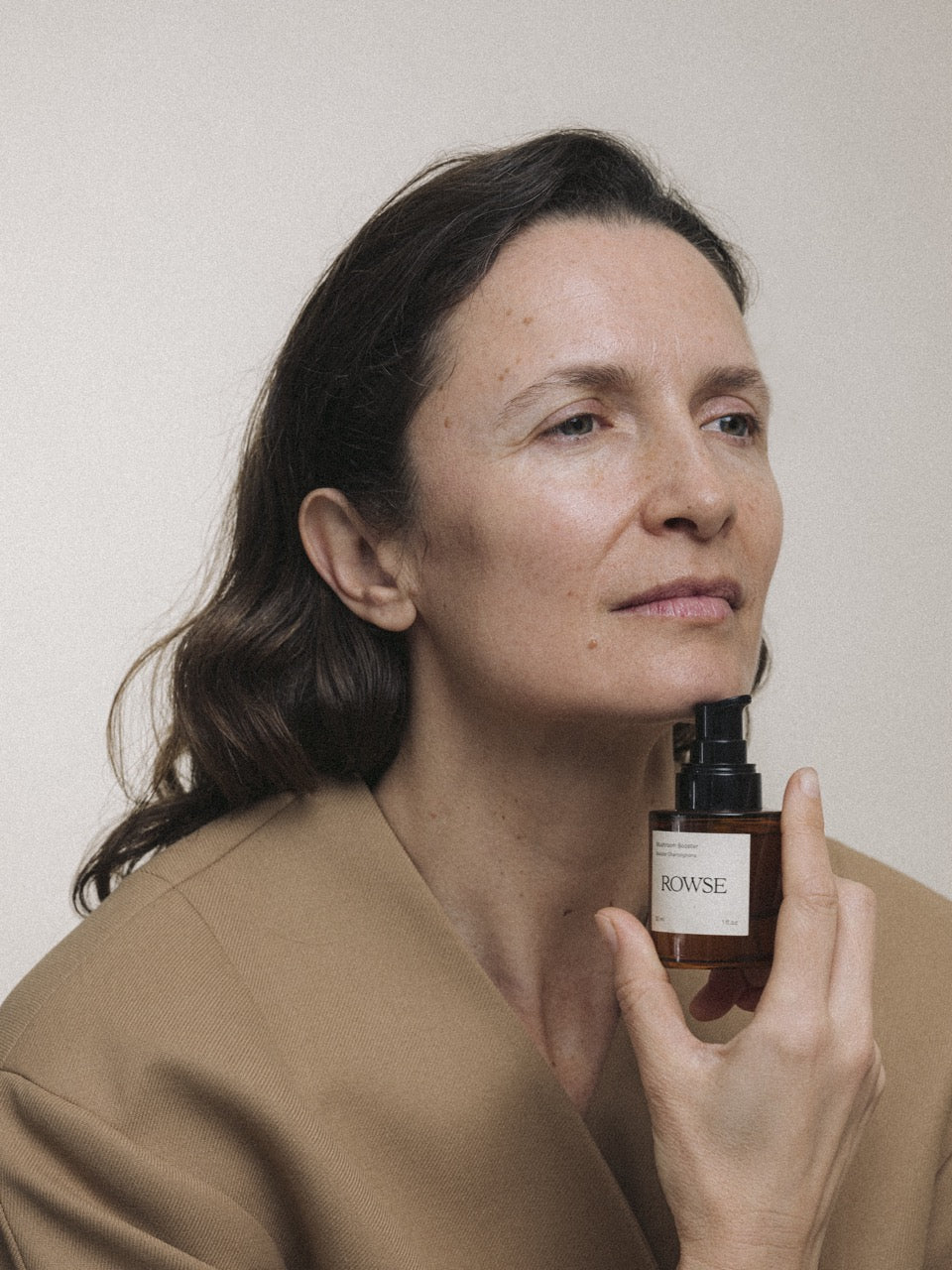 ROWSE skincare booster serum held by a mature woman in neutral tones, showcasing natural, minimalist beauty and skincare elegance
