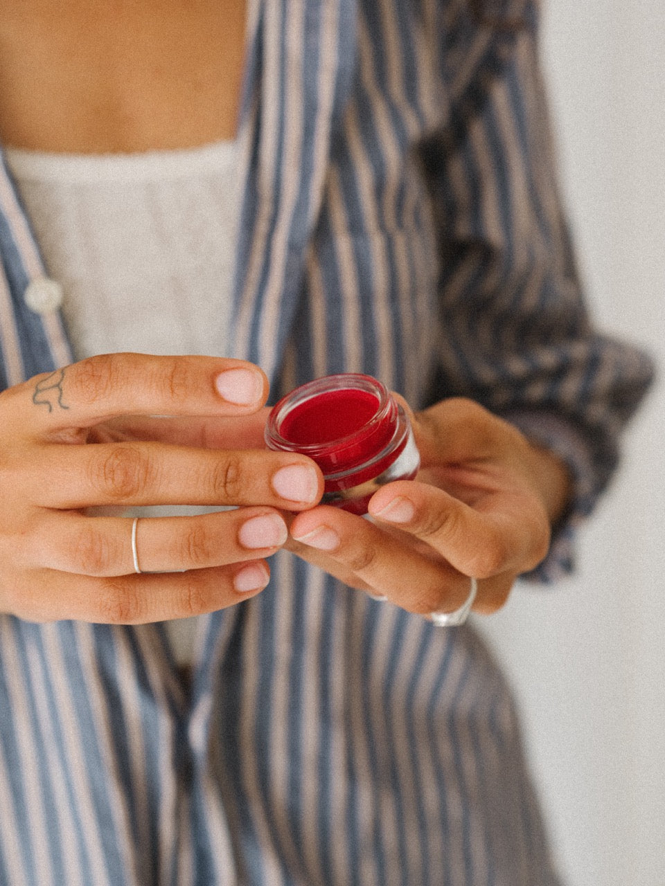 ROWSE Summer Blush Lip & Cheek Balm in vibrant red shade, held delicately in hands with striped shirt styling, showcasing multi-use beauty product