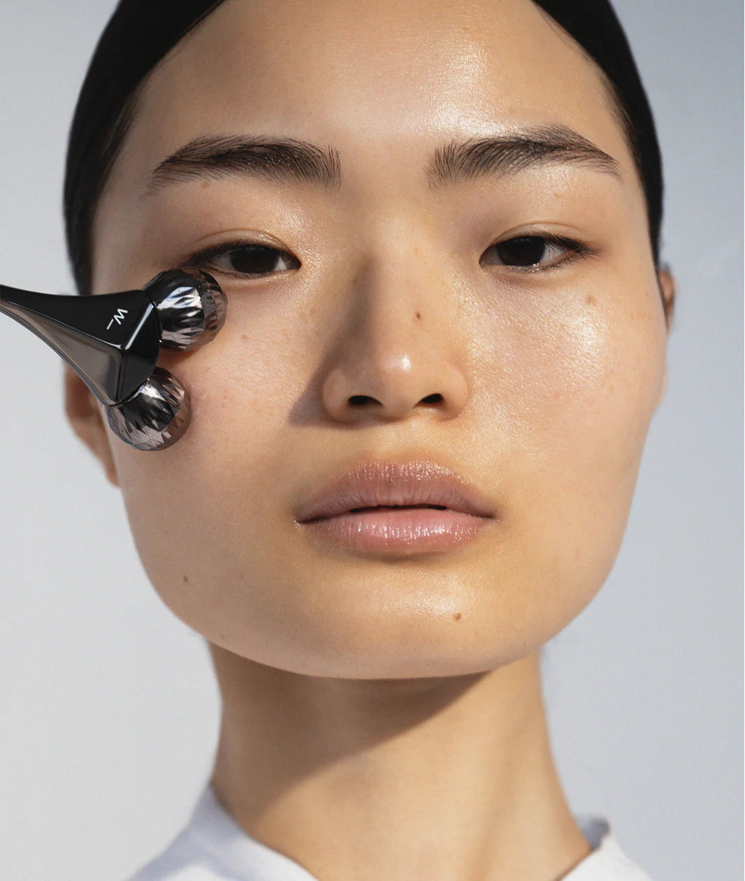 Woods Copenhagen Contouring Roller applied on young model's face, demonstrating precise facial massage technique with metallic textured roller heads