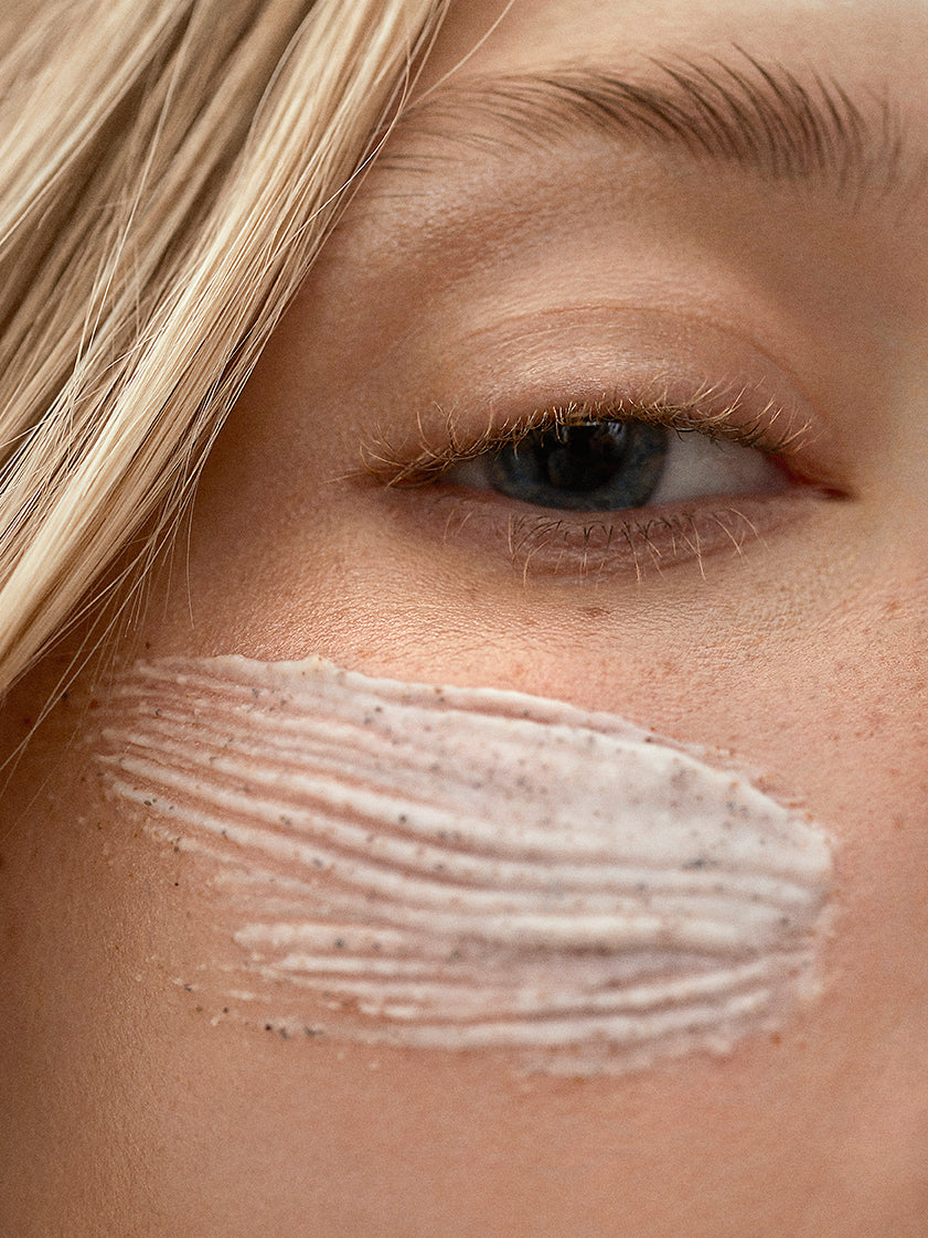Close-up of Woods Copenhagen deep cleansing scrub applied on skin, showcasing gentle exfoliation texture with natural, granular particles against soft, neutral skin tone