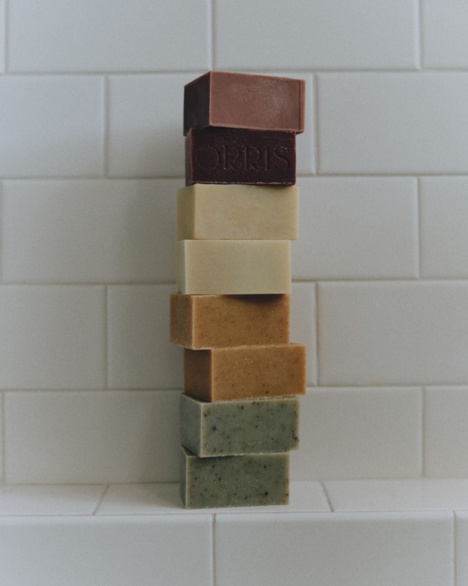 Orris natural soap bars stacked on white bathroom tiles
