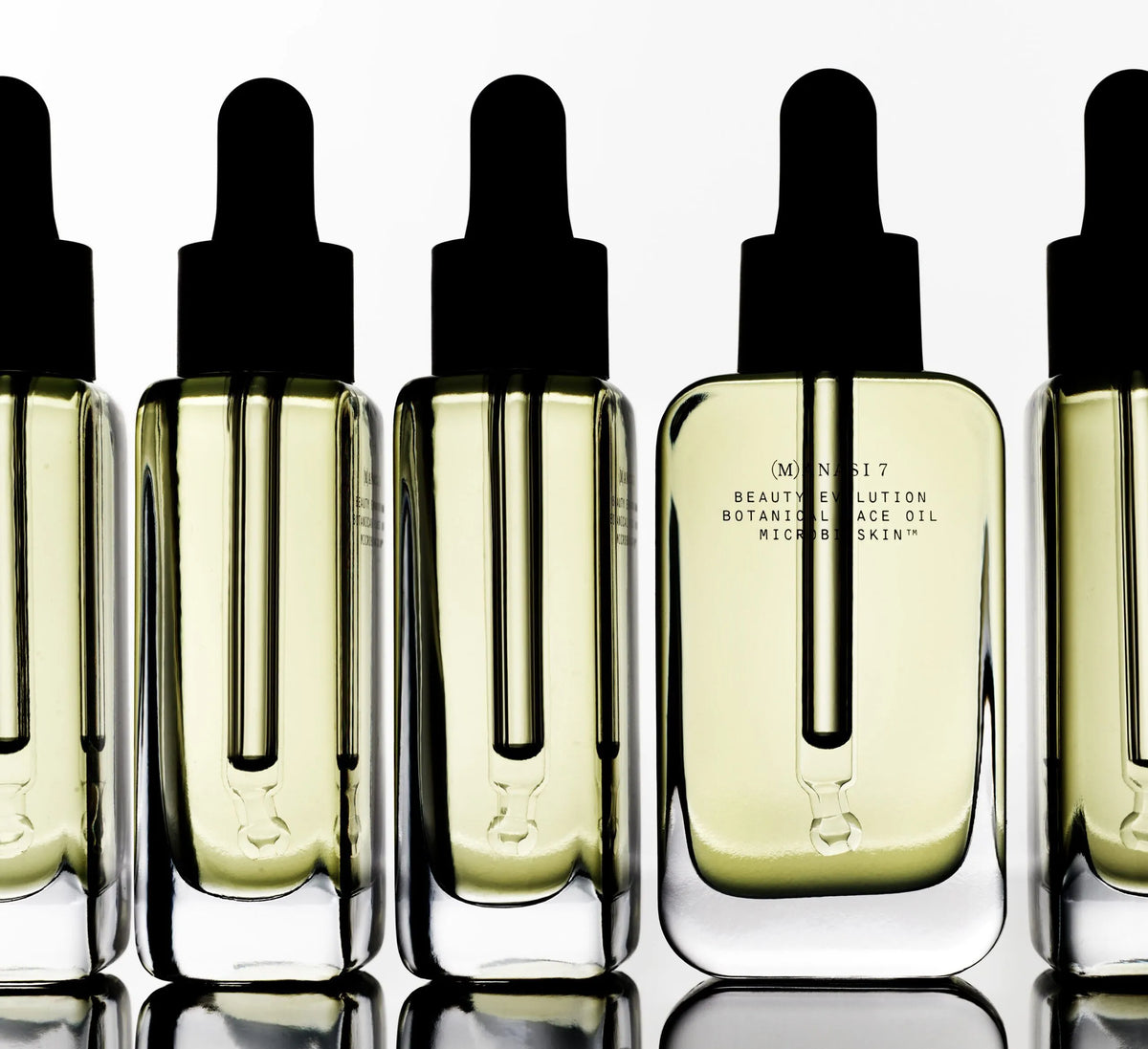 Manasi 7 Beauty Balm Miel Botanique face oil bottles with dropper caps on a reflective white surface