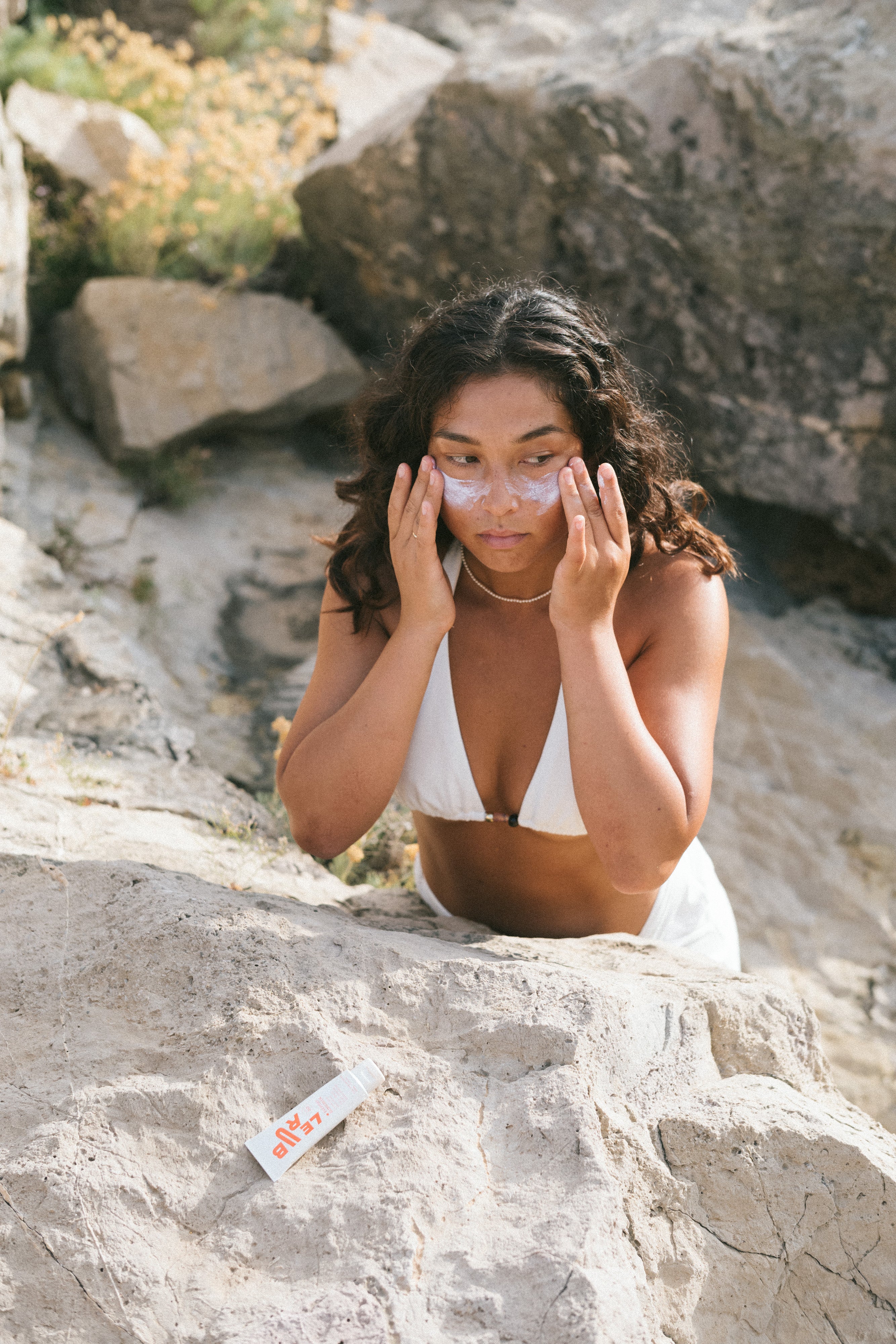 Sunscreen application in natural rocky beach setting, showcasing skincare routine with minimalist, editorial aesthetic