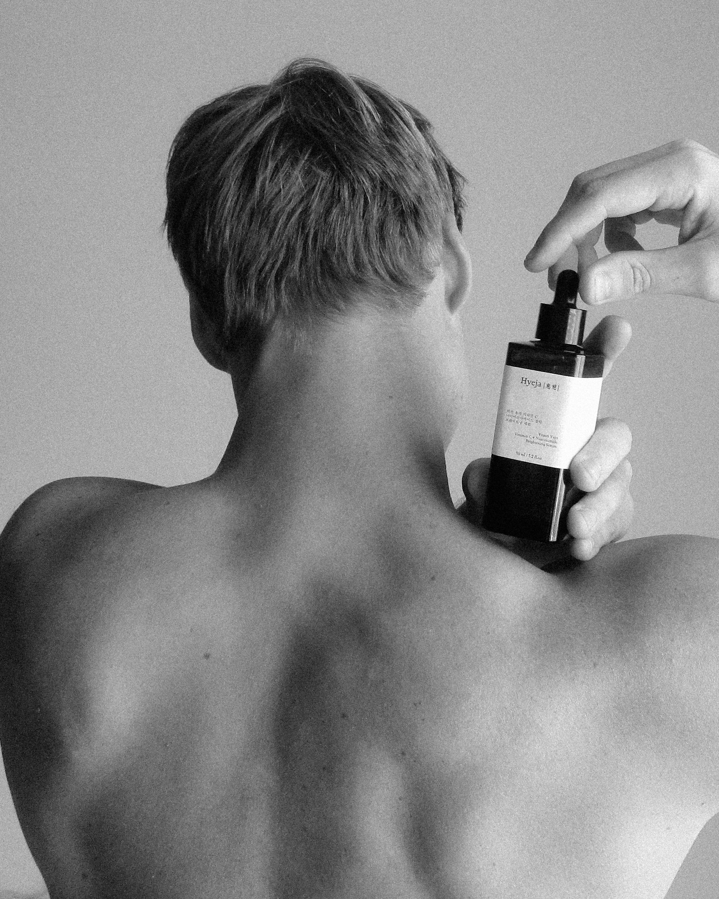 Black and white image of a person's back, holding Hyeja Vitamin C Serum, showcasing minimalist skincare photography with editorial styling