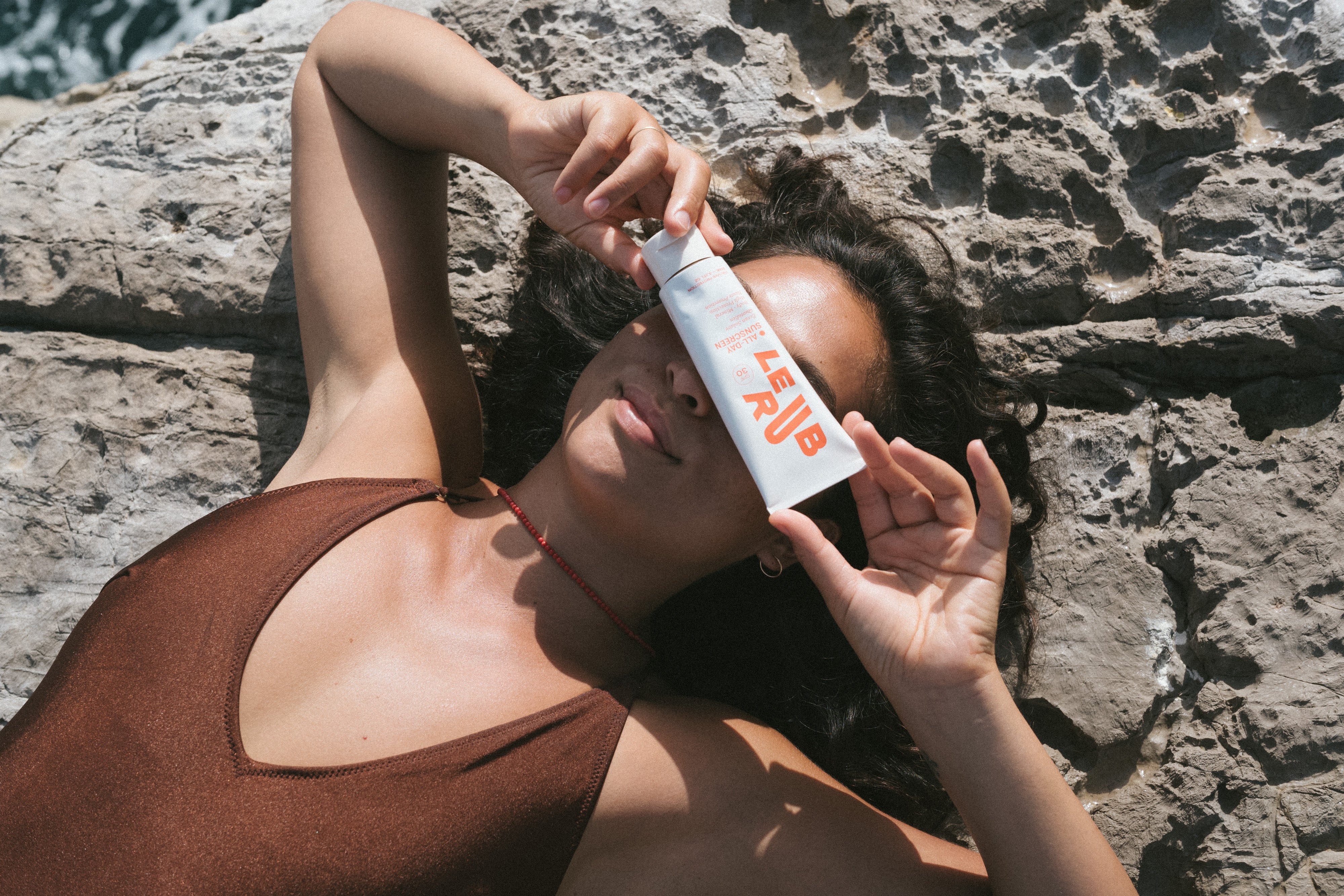 Le Rub suncare lifestyle image - Woman confidently holding all-day sun protection, embodying coastal wellness and skin defense