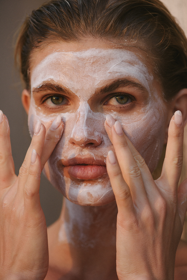 Woman applying Le Rub repairing face mask in natural outdoor setting, showcasing skincare routine with minimalist, editorial aesthetic