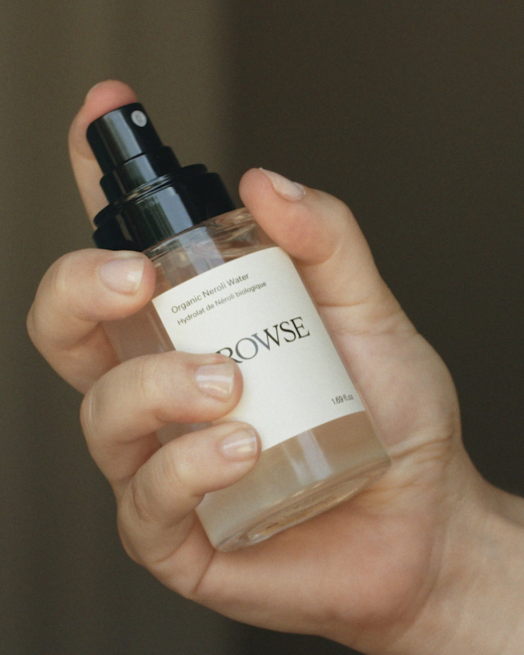 ROWSE Organic Rose Water Hydrolat being applied, demonstrating gentle toning and hydrating skincare technique with natural botanical backdrop
