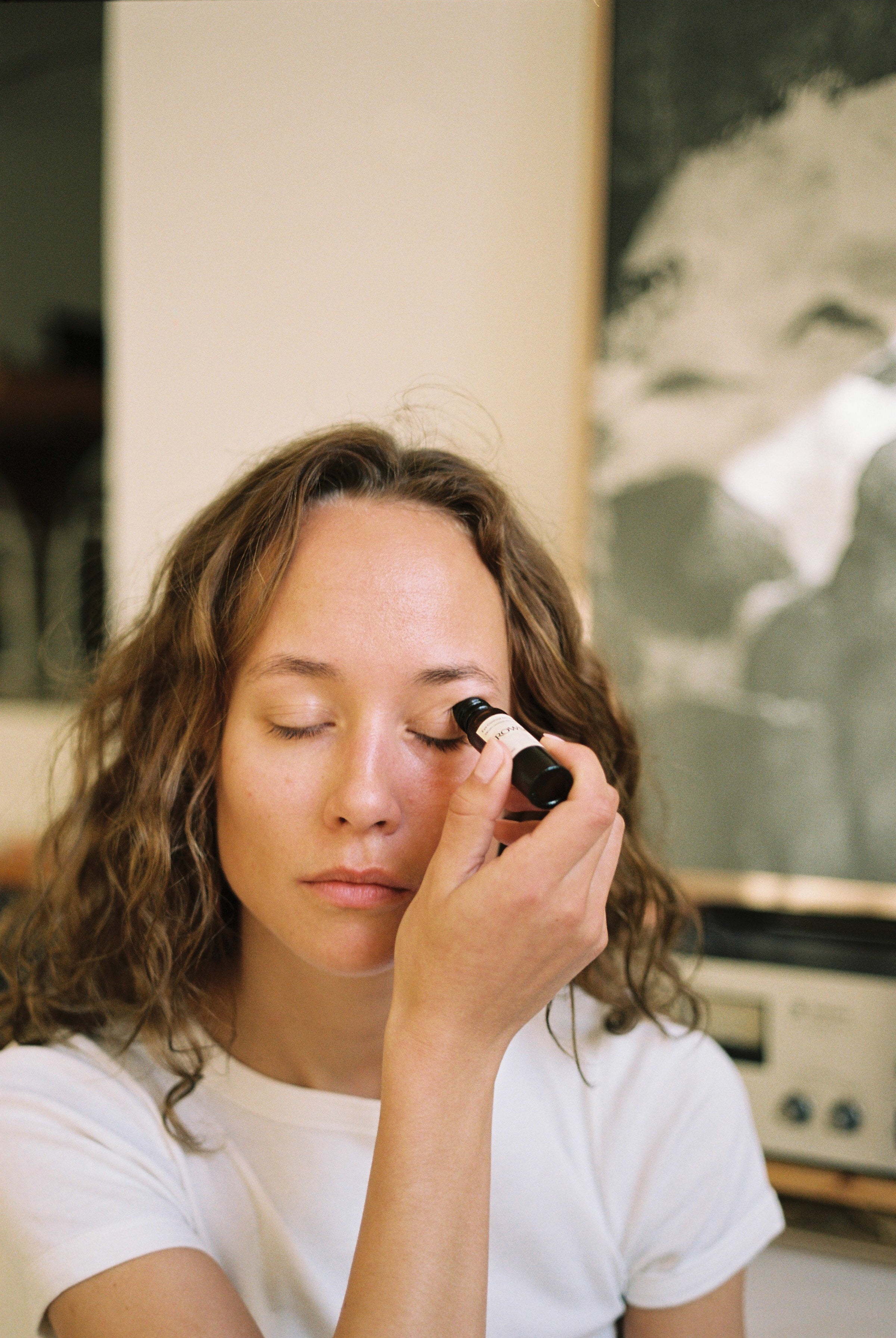 ROWSE eye serum being applied with a roller, showcasing a gentle skincare routine with a person's eyes closed in a calm, natural setting
