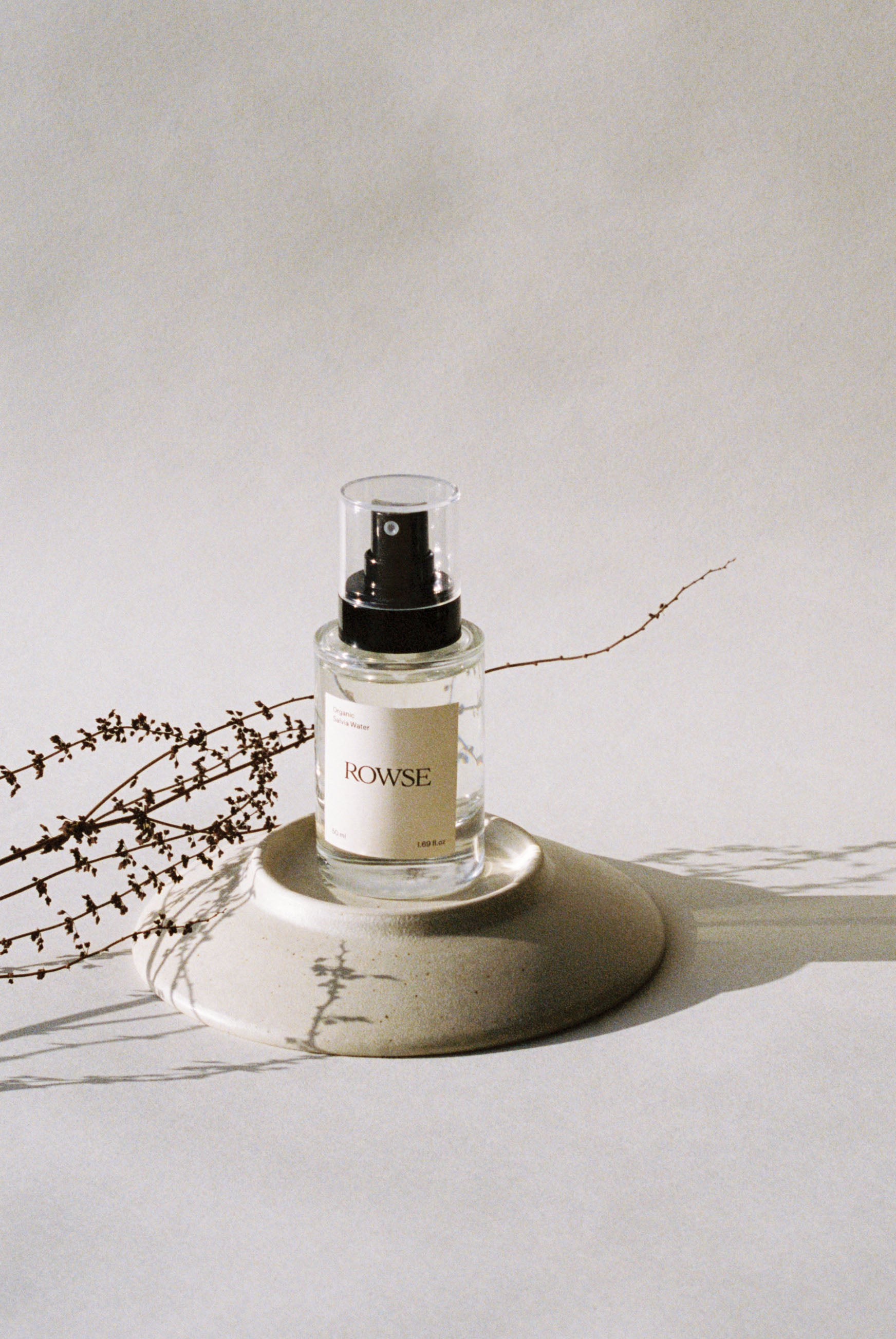 ROWSE Organic Rose Water spray bottle positioned on a ceramic plate with dried botanical branches, showcasing minimalist skincare aesthetic with natural styling