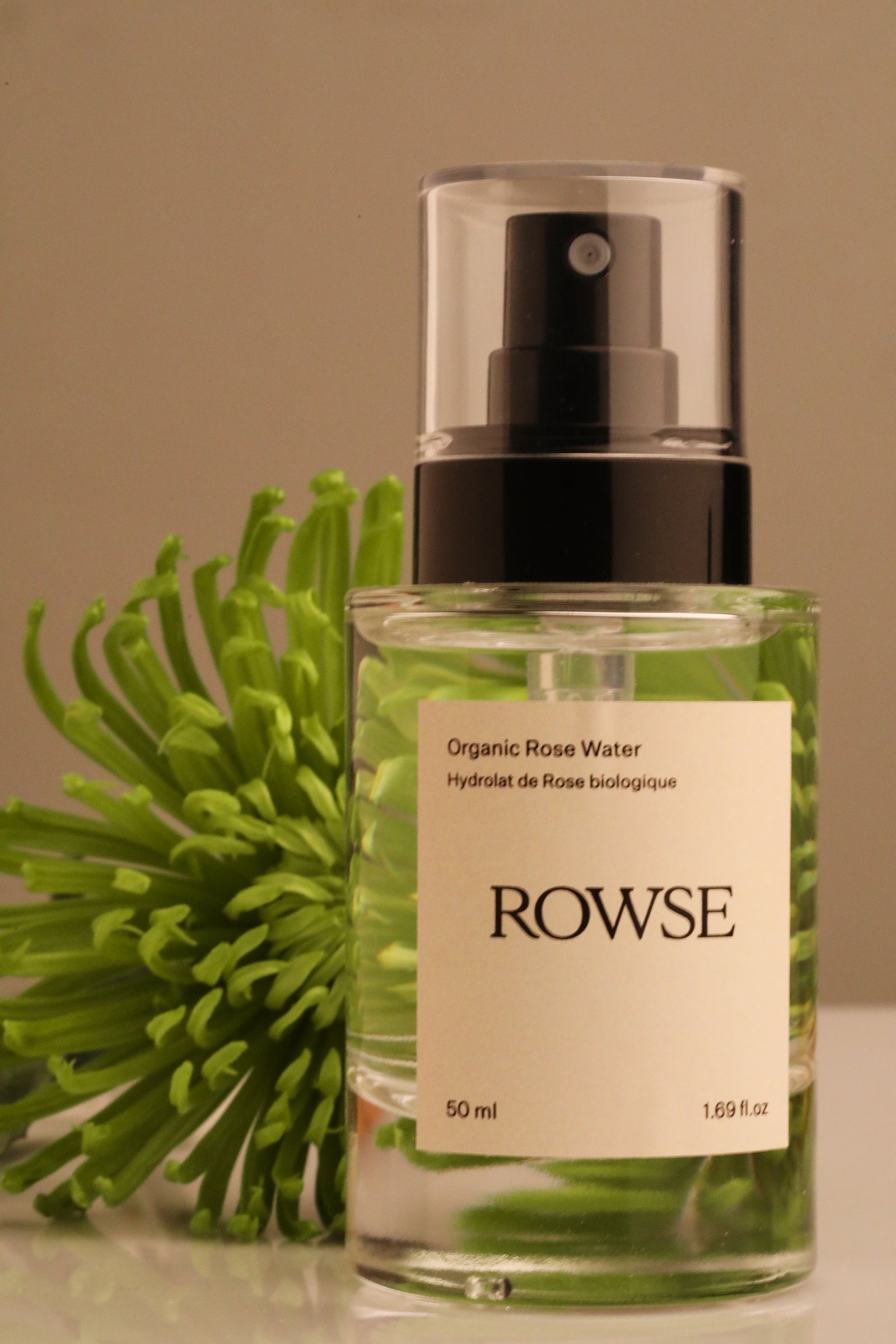 ROWSE Organic Rose Water Hydrolat, 50ml spray bottle positioned with vibrant green botanical flower, showcasing natural skincare and clean beauty aesthetic
