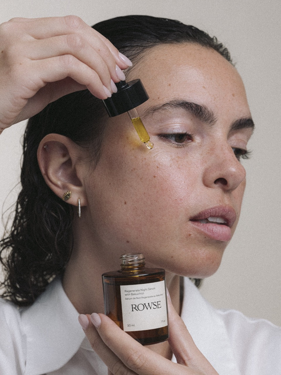 ROWSE Regenerate Night Serum with Bakuchiol being applied to face, showcasing golden oil droplet and intimate skincare ritual with natural, editorial styling
