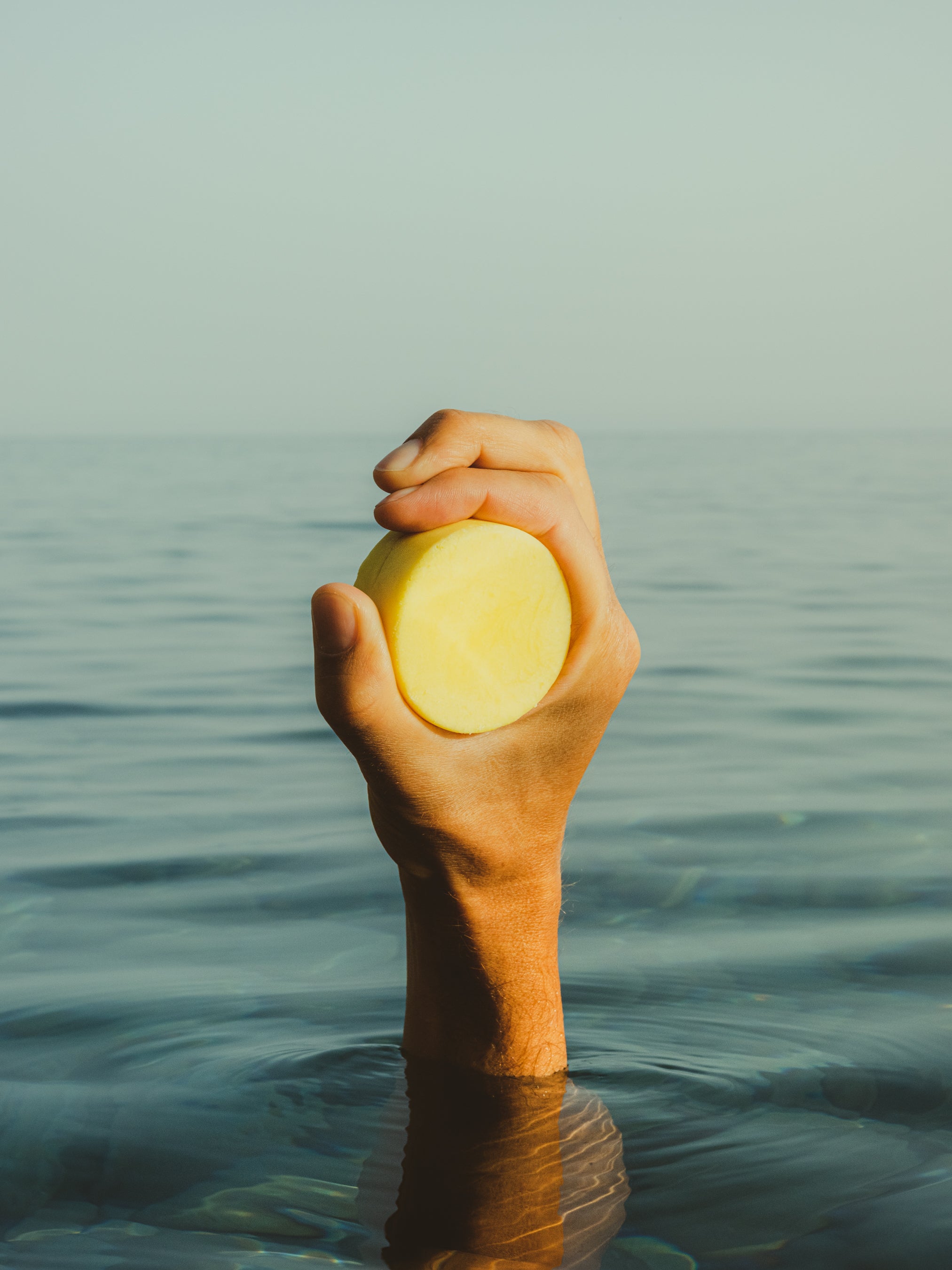 ROWSE solid shampoo bar held above water, showcasing sustainable hair care product with minimalist, editorial styling
