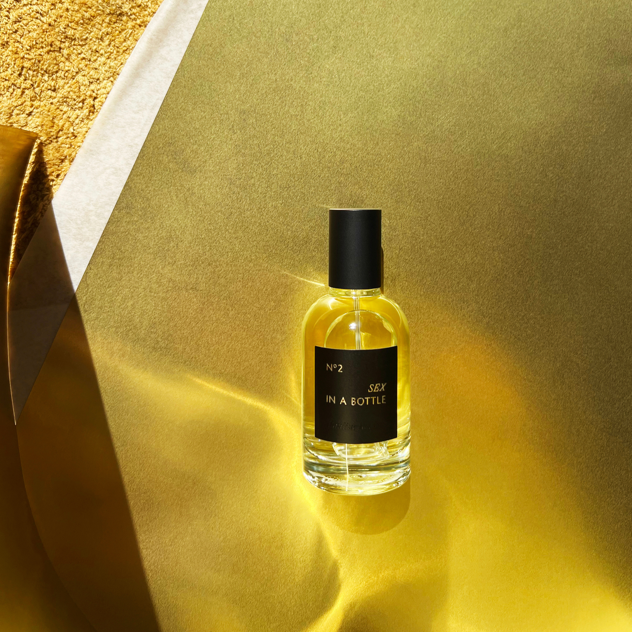 Sex in a Bottle No2 perfume in glass bottle, showcasing dramatic golden lighting and minimalist packaging design

