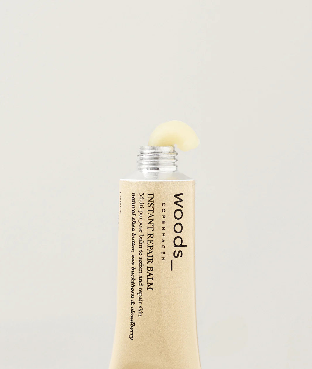 Woods Copenhagen Instant Repair Balm emerging from tube, showcasing creamy texture and minimalist Scandinavian skincare packaging design